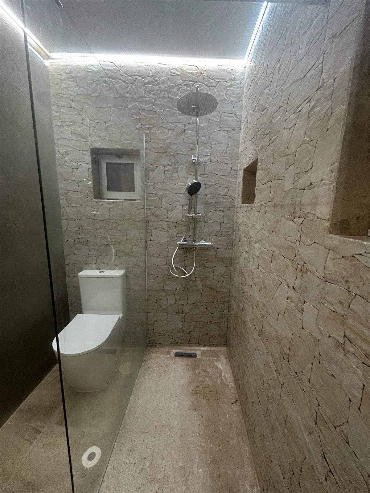 A second finished stone-clad bathroom with a tall walk-in shower, rain head and full stone walls, renovated by Justin Sterrenberg on the Silver Coast