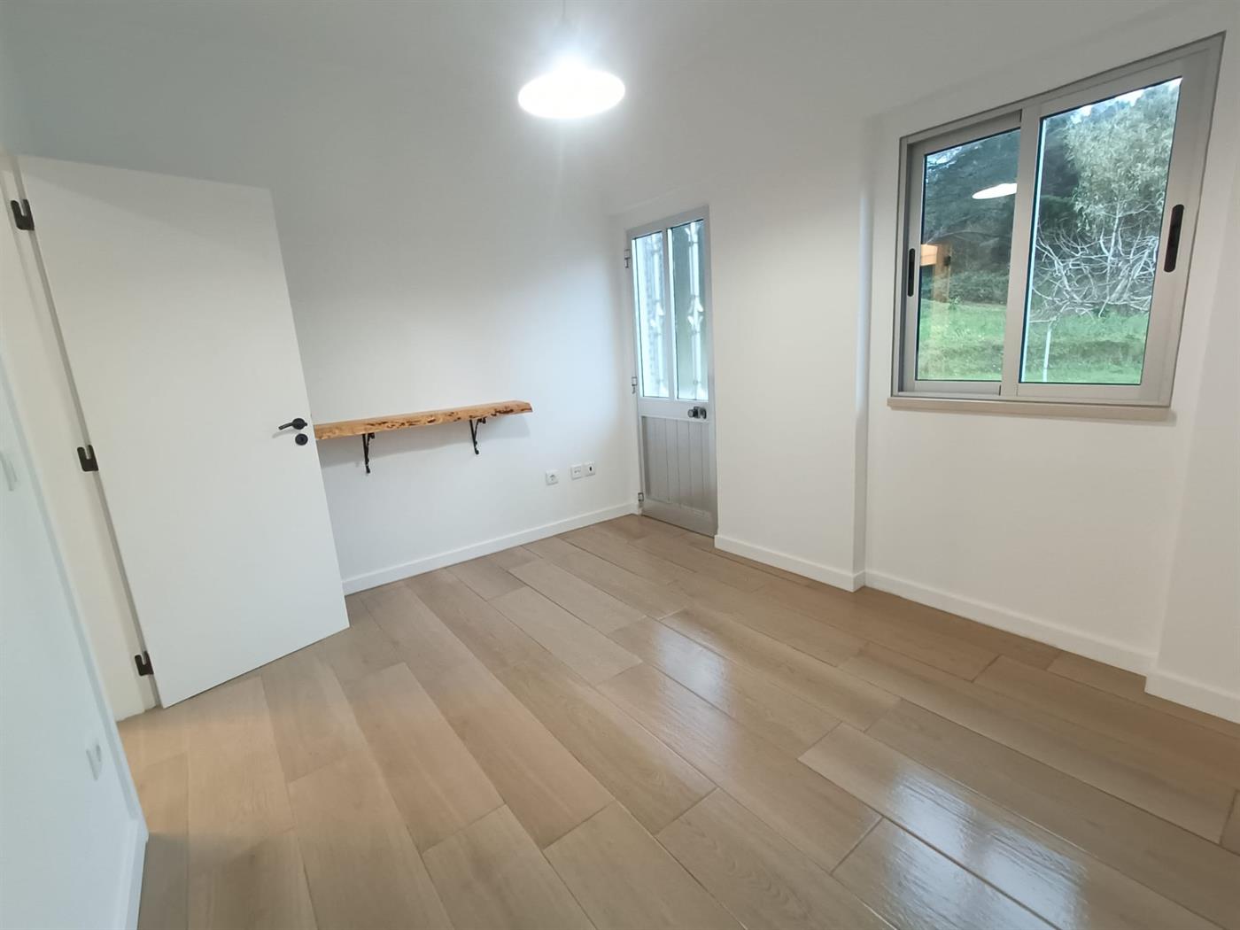 A freshly renovated interior room with white walls, light oak flooring, a live-edge timber shelf and a large window, finished by Justin Sterrenberg on the Silver Coast