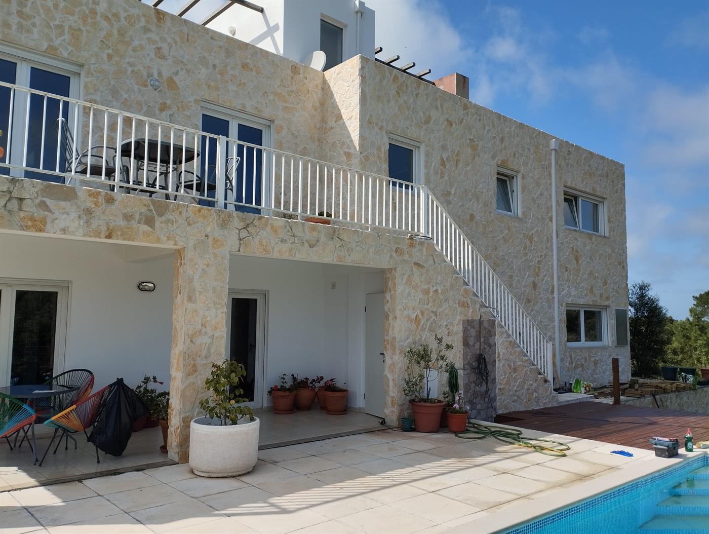 A two-storey Silver Coast villa with full natural-stone cladding, white-railed upper terrace and external staircase, finished by Michael Straub